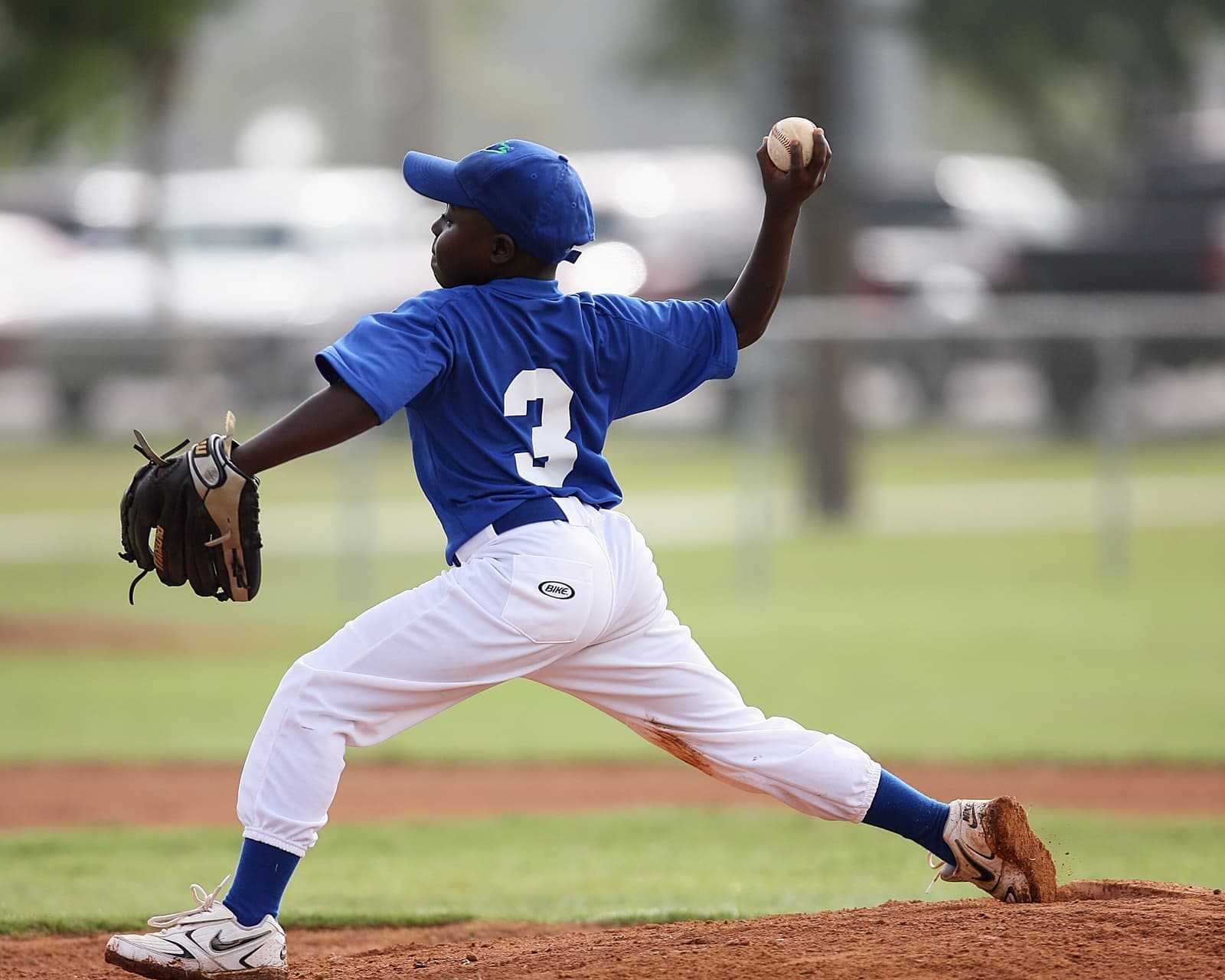 A young player pitching in a youth baseball game on a sunny day