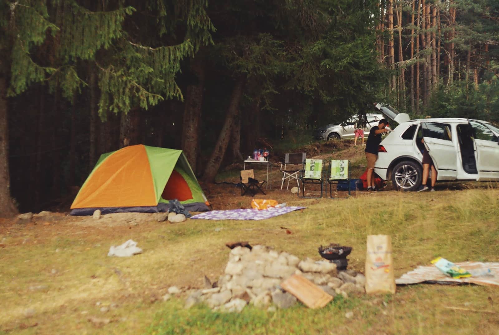 A forest campsite with a tent, a car and a campfire