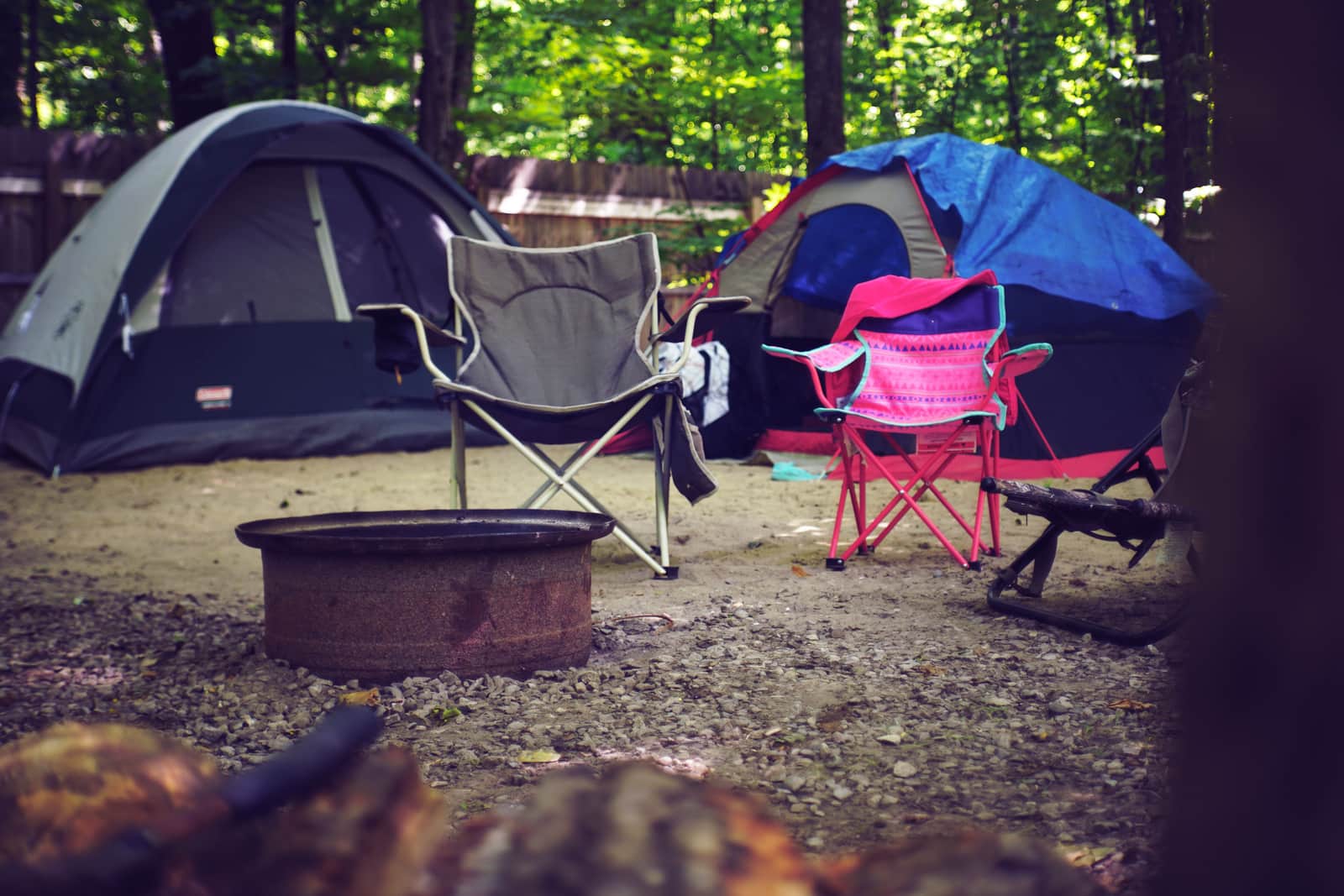A wooded campsite with tents, camping chairs and a fire pit