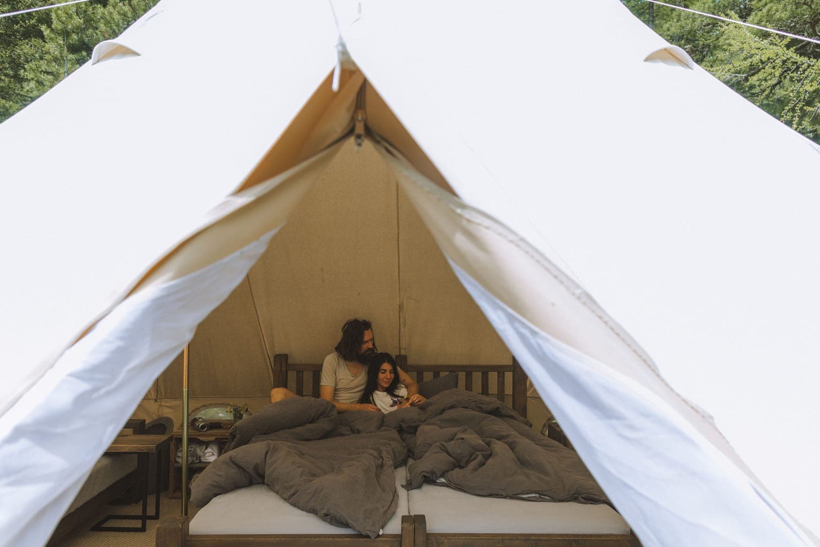 A couple resting on a raised bed inside an open canvas bell tent